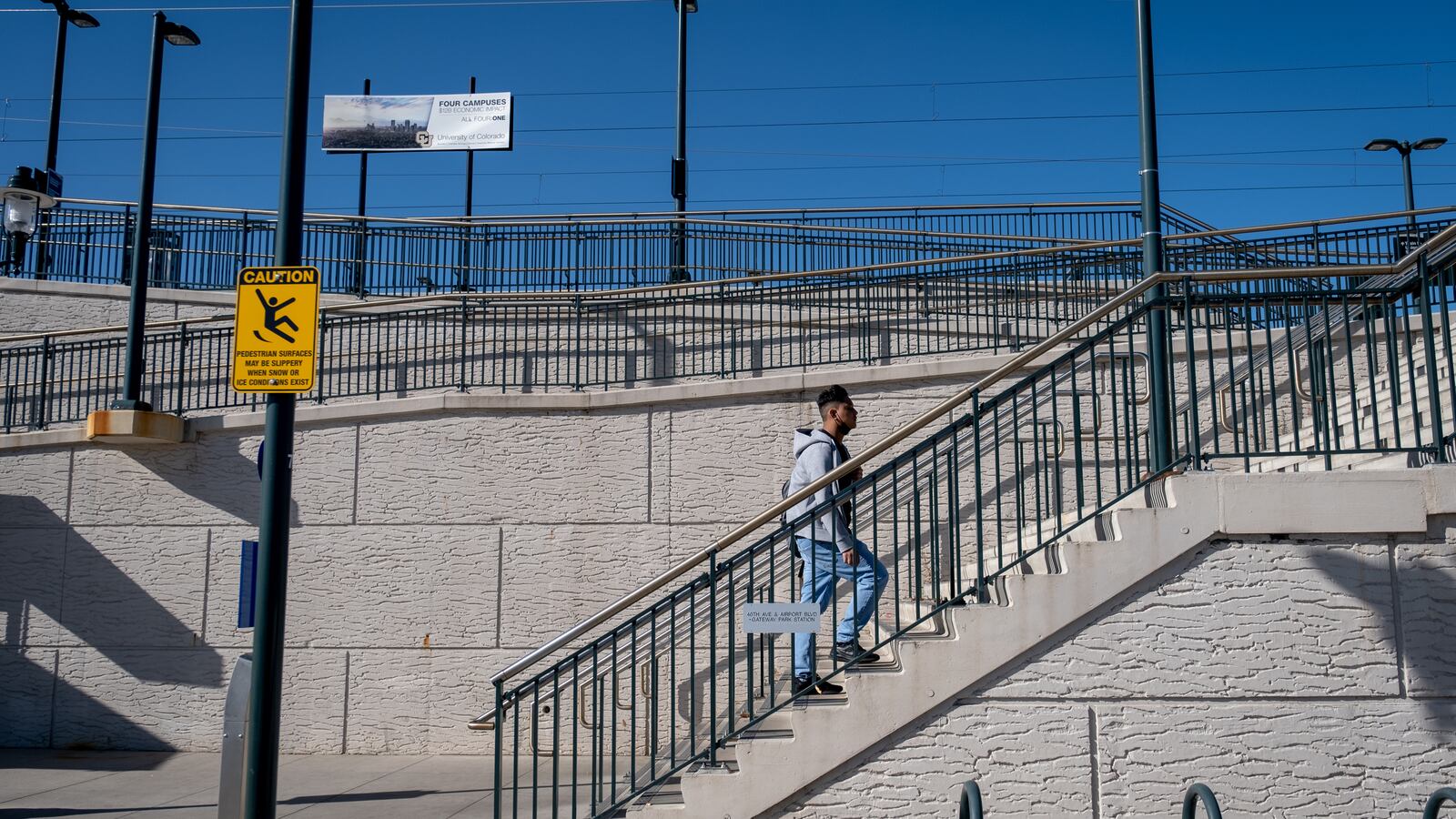 A young man, wearing jeans and a grey sweatshirt, walks up a staircase toward a train station.