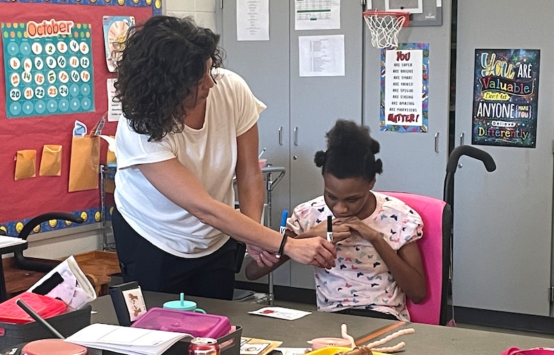 A teacher works with a student inside a classroom.