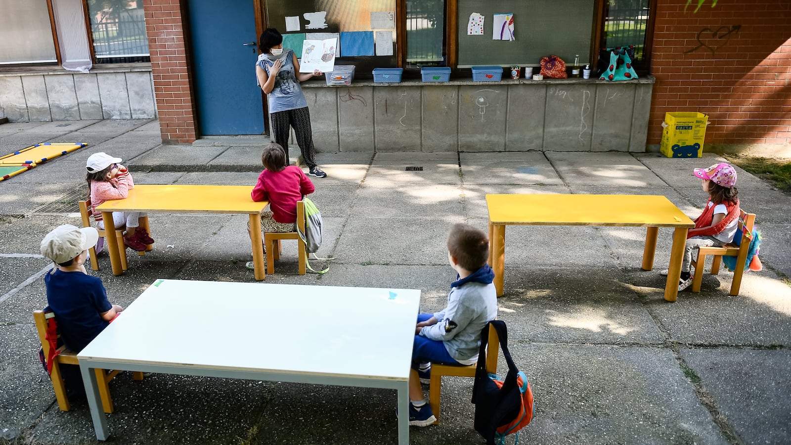 A teacher reads a book to kindergarten children in a school...