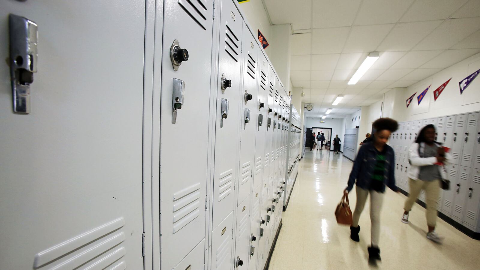 Students walk past white lockers in a school hallway