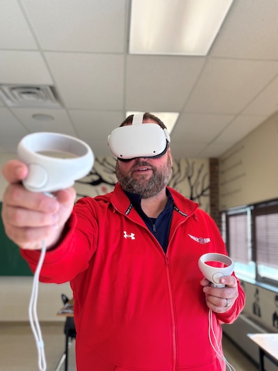 A photograph of a man in a red jacket with virtual reality goggles on.