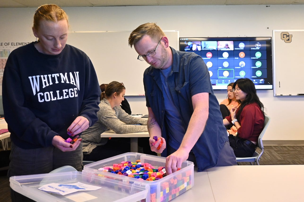 Two students work with colorful pieces at a table.