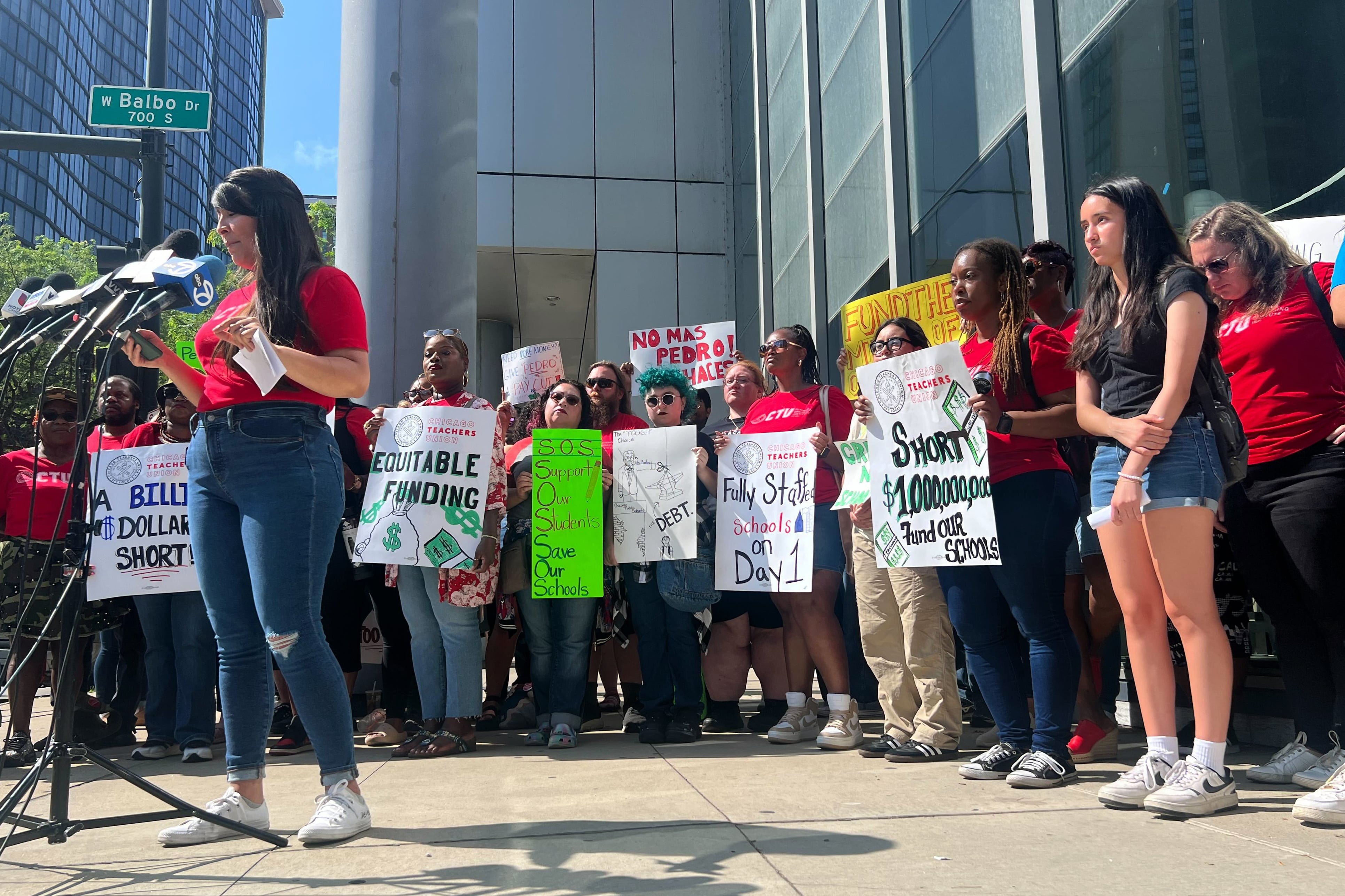 A group of people mostly wearing red t-shirts gather outside in front of a building.