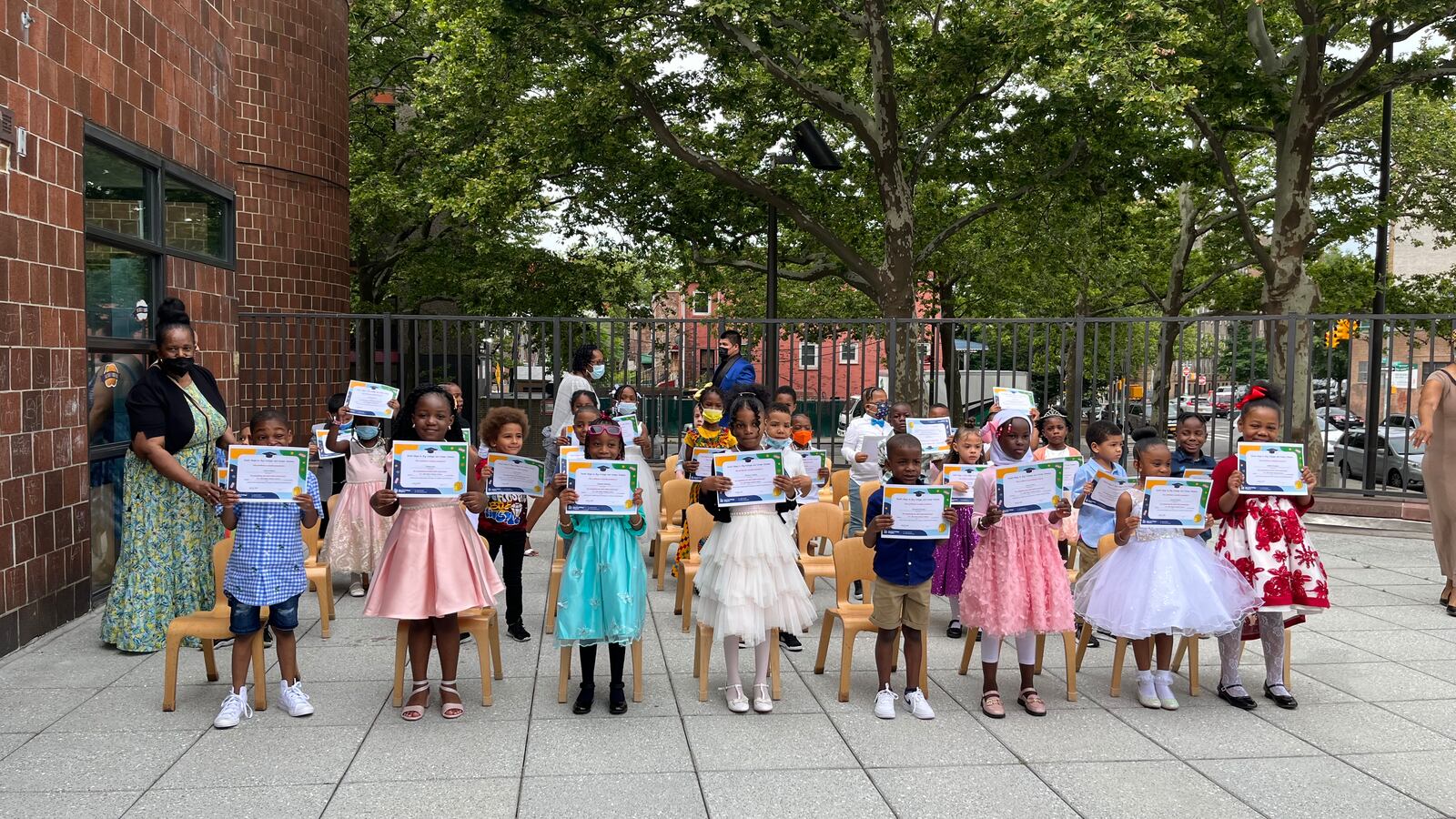 A group of kindergarten children at a graduation ceremony, the girls wearing pastel-colored princess dresses.