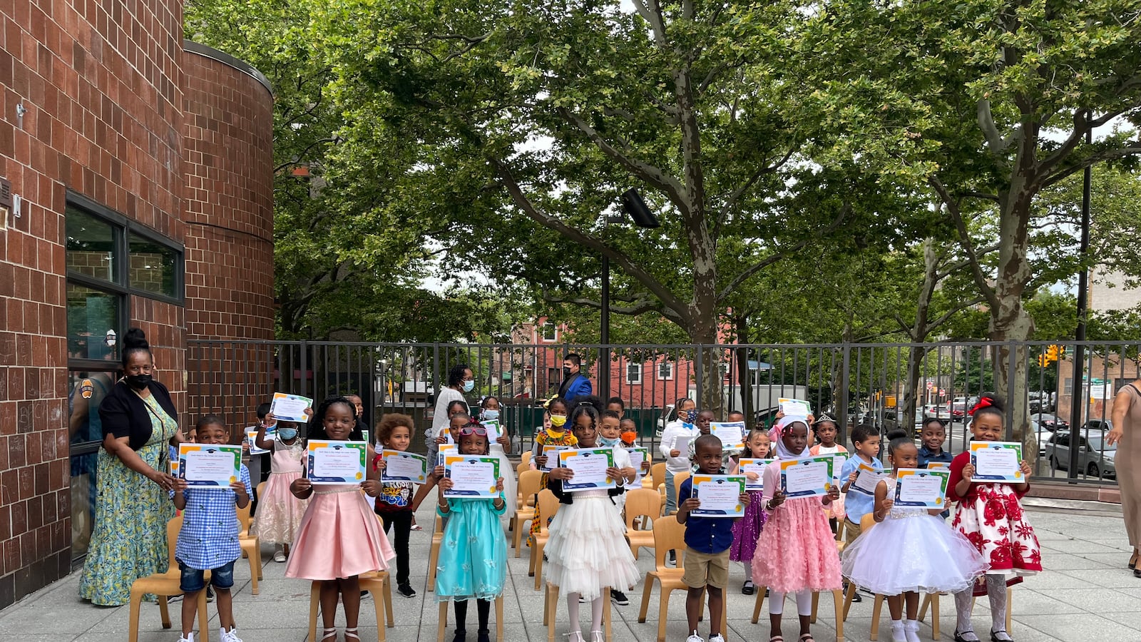 A group of kindergarten children at a graduation ceremony, the girls wearing pastel-colored princess dresses. 