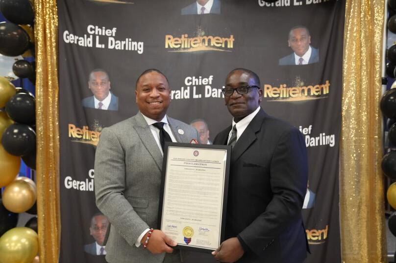 Two men wearing suits pose with a certificate at a retirement party