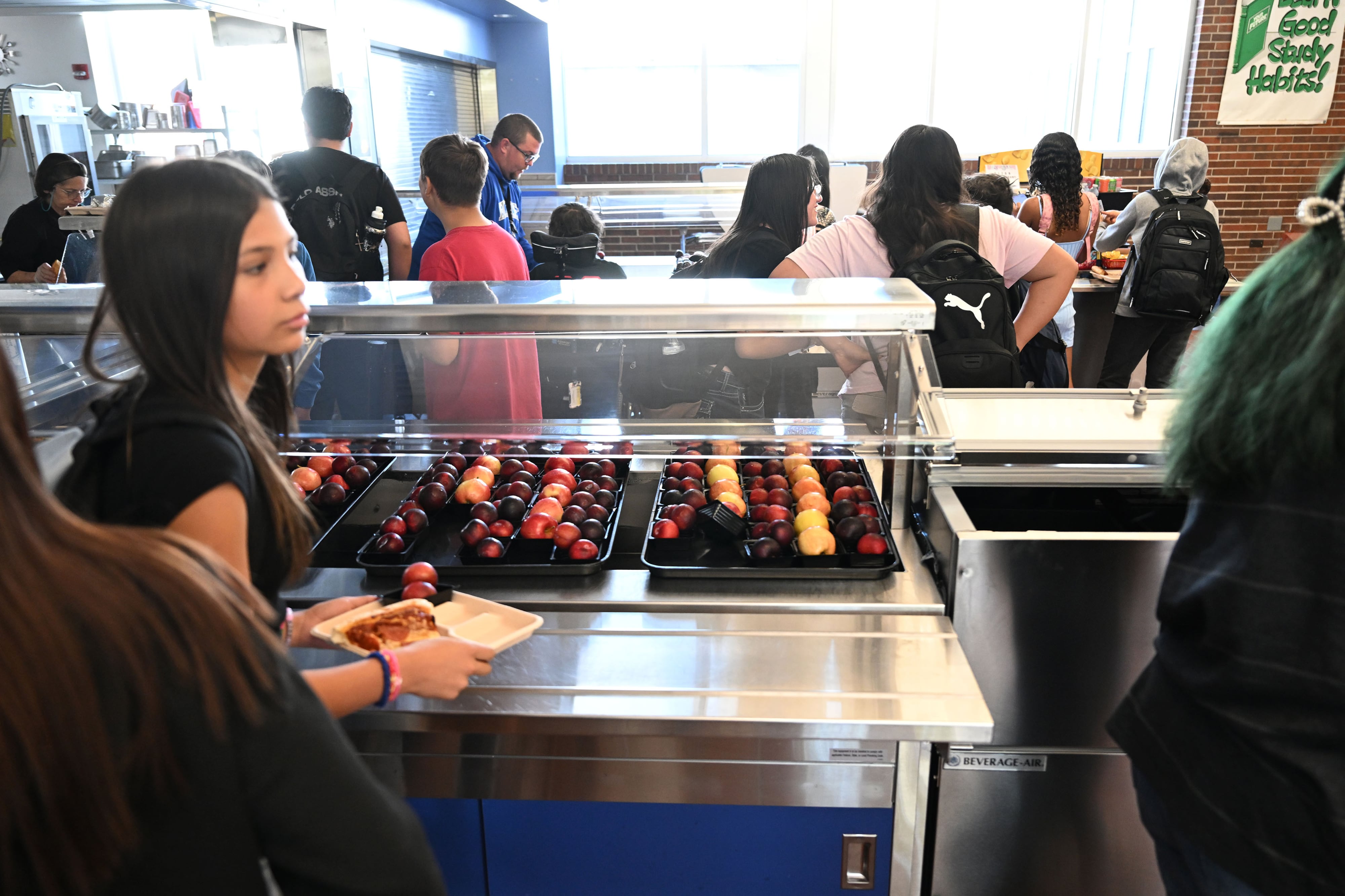 A school cafeteria full of students and a food bar full of apples.