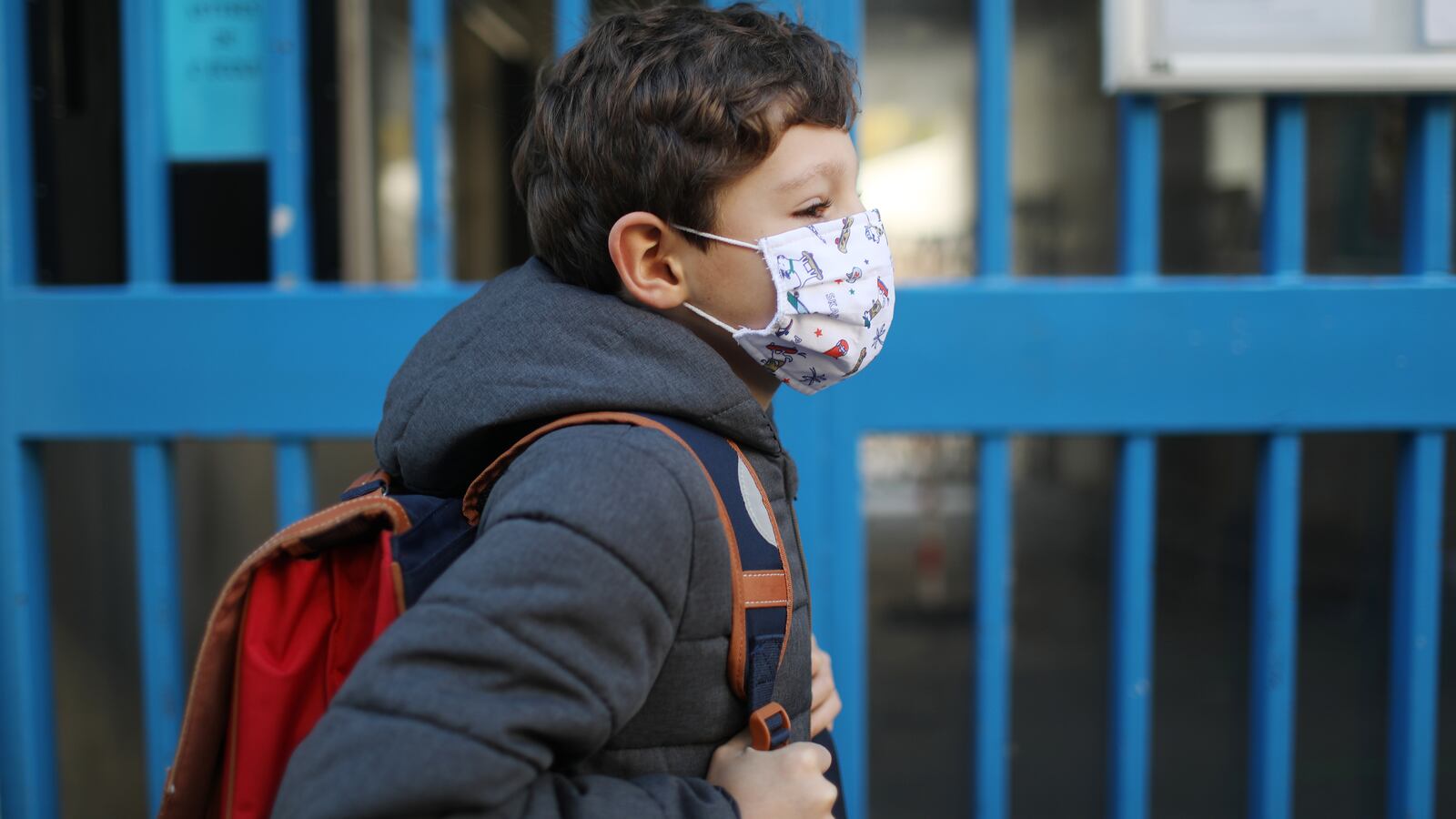 Child wearing a dark sweatshirt, orange backpack, and protective face mask walks to school during COVID-19 pandemic
