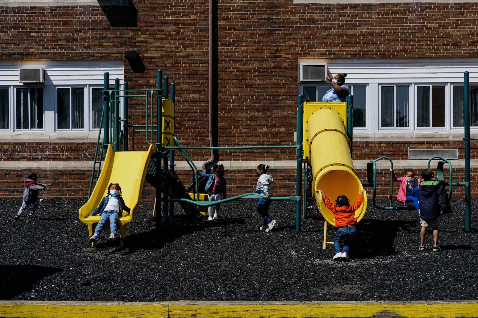 Children play on a yellow slide set on the side of a school building.