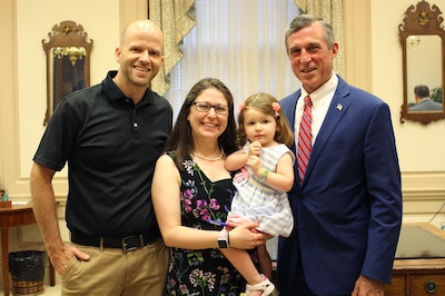A photograph of three adults and one woman holding a toddler.