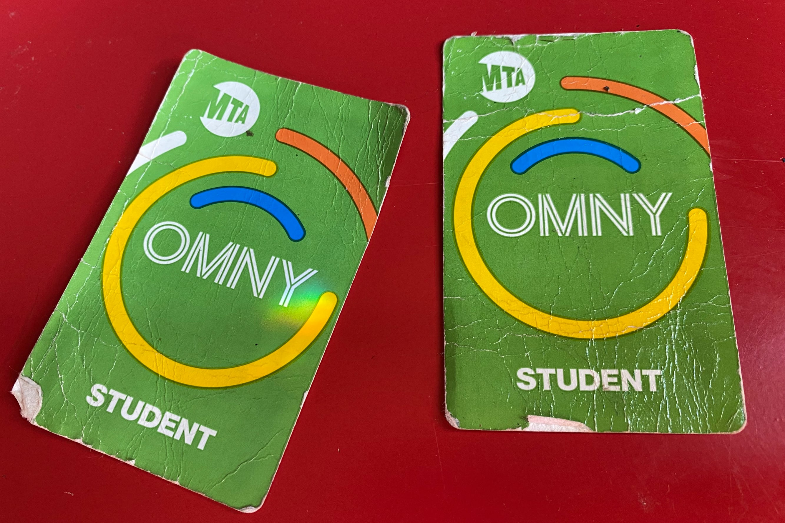 A photograph of two green OMNY student transportation cards on a red background.