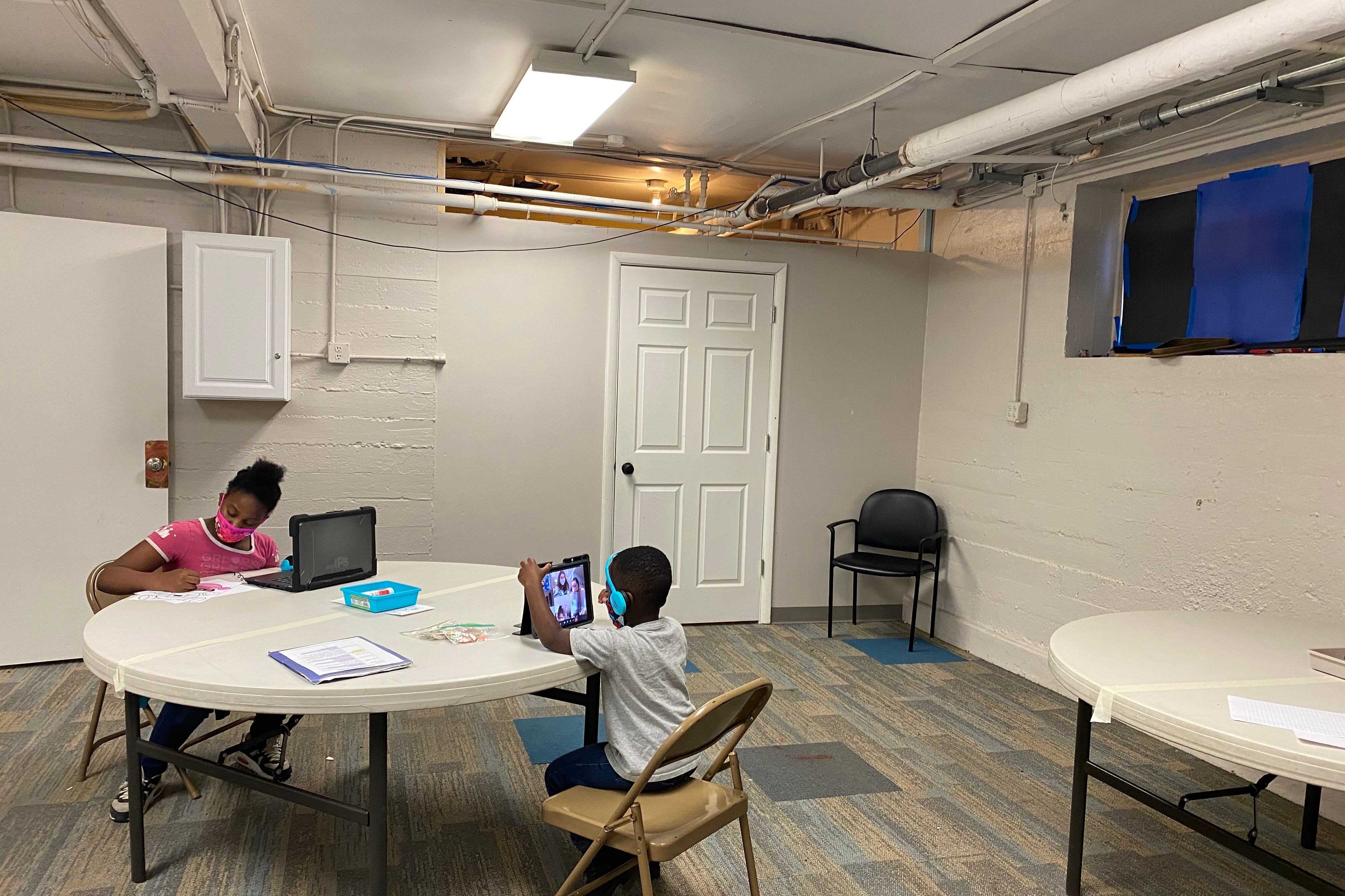 Two students sit at a round table working on laptops and tablets, working on virtual lessons in Indianapolis, Ind.