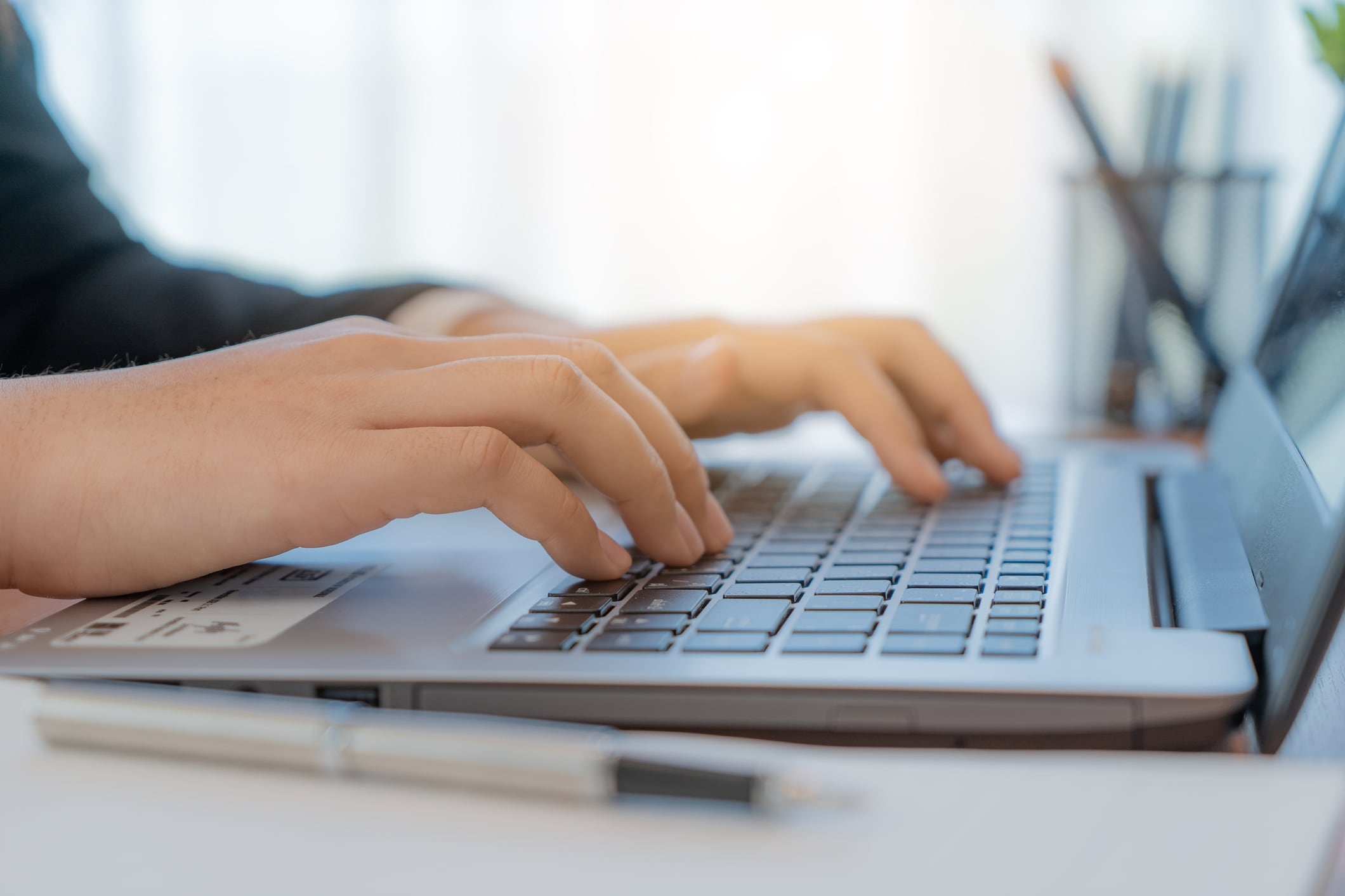 Close-up of hands using modern laptop in office, businesswoman in suit working on notebook computer in a room.