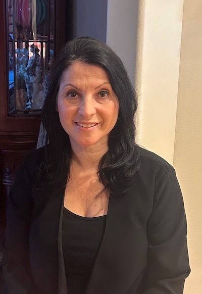 A woman with medium length dark hair and wearing a dark sweater smiles at the camera.