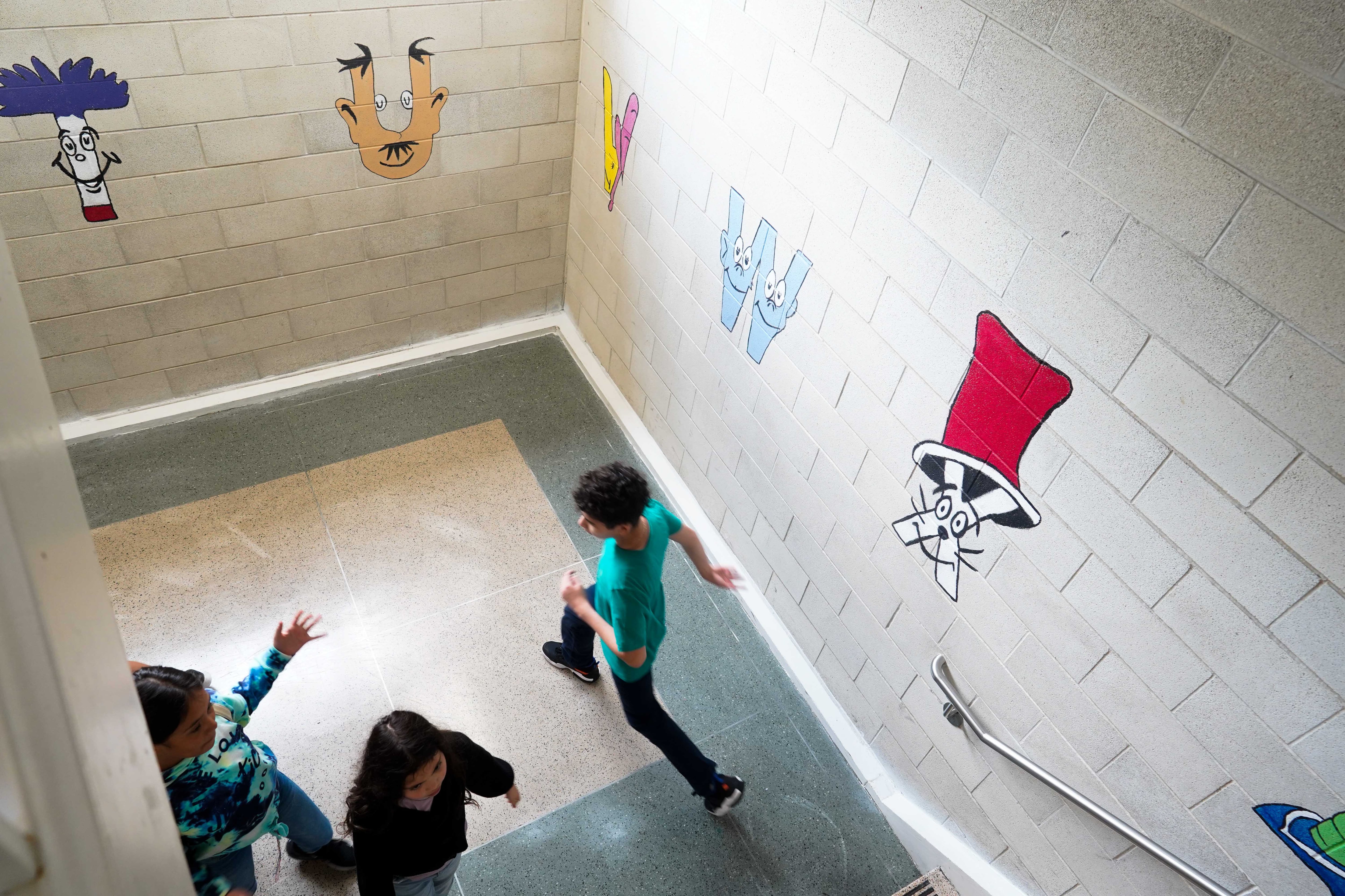 Students run in a stairwell decorated with letters with faces.