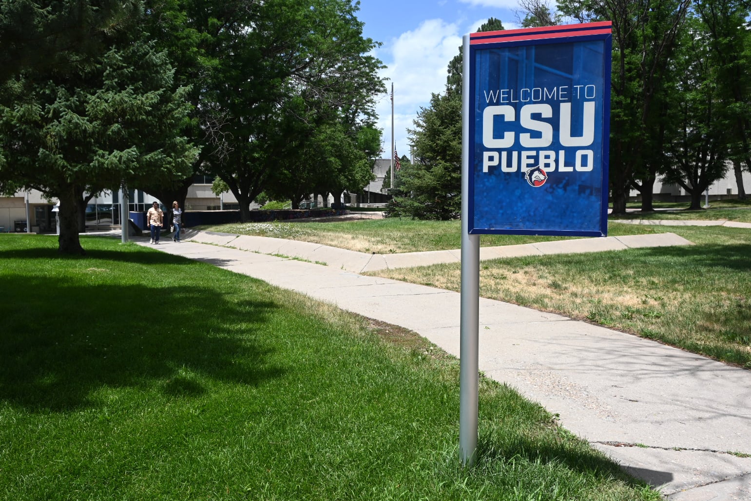 A banner hangs on a pole on a scenic campus.