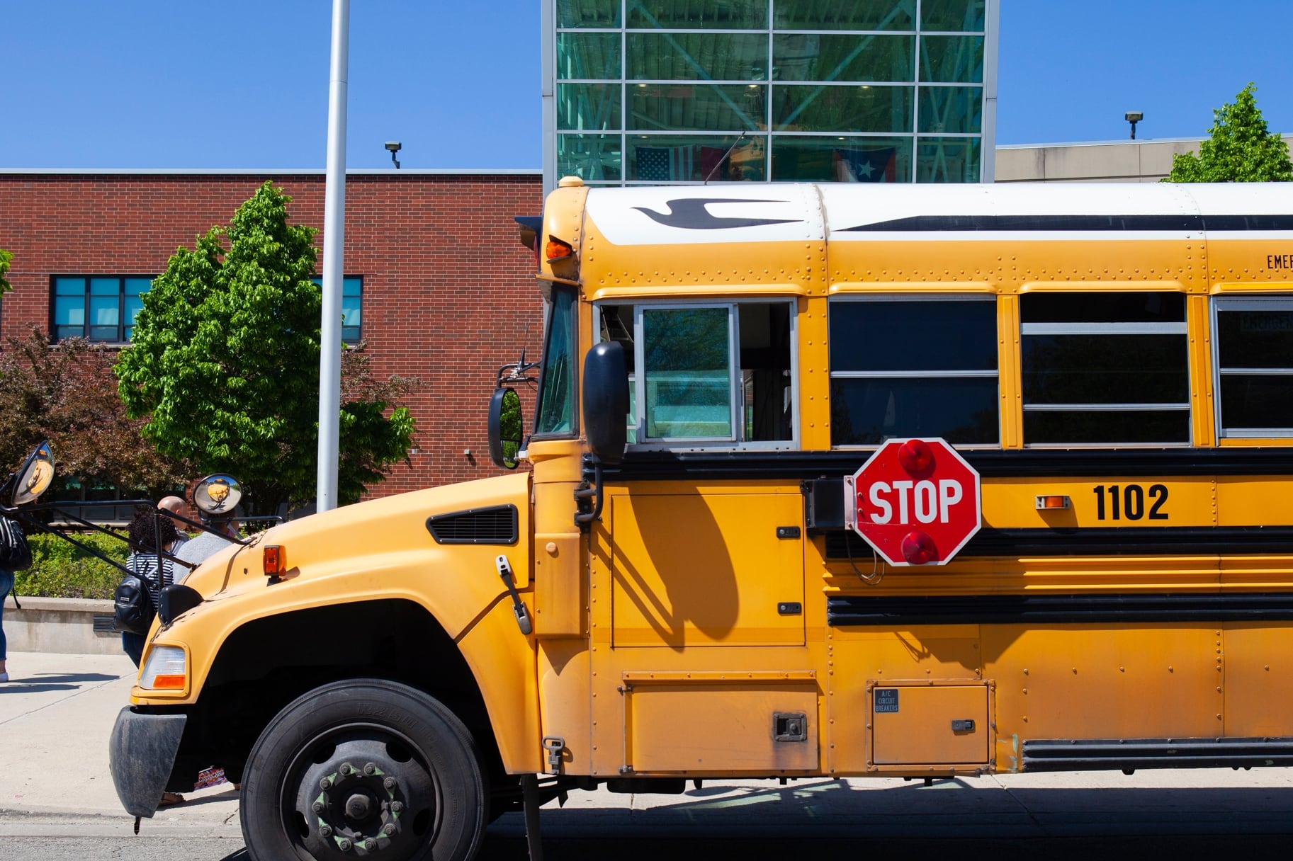 A yellow school bus is parked near the front entrance of a school building.