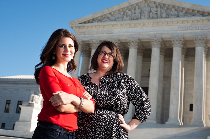 Two women stand in front of the Supreme Court and smile for a portrait.