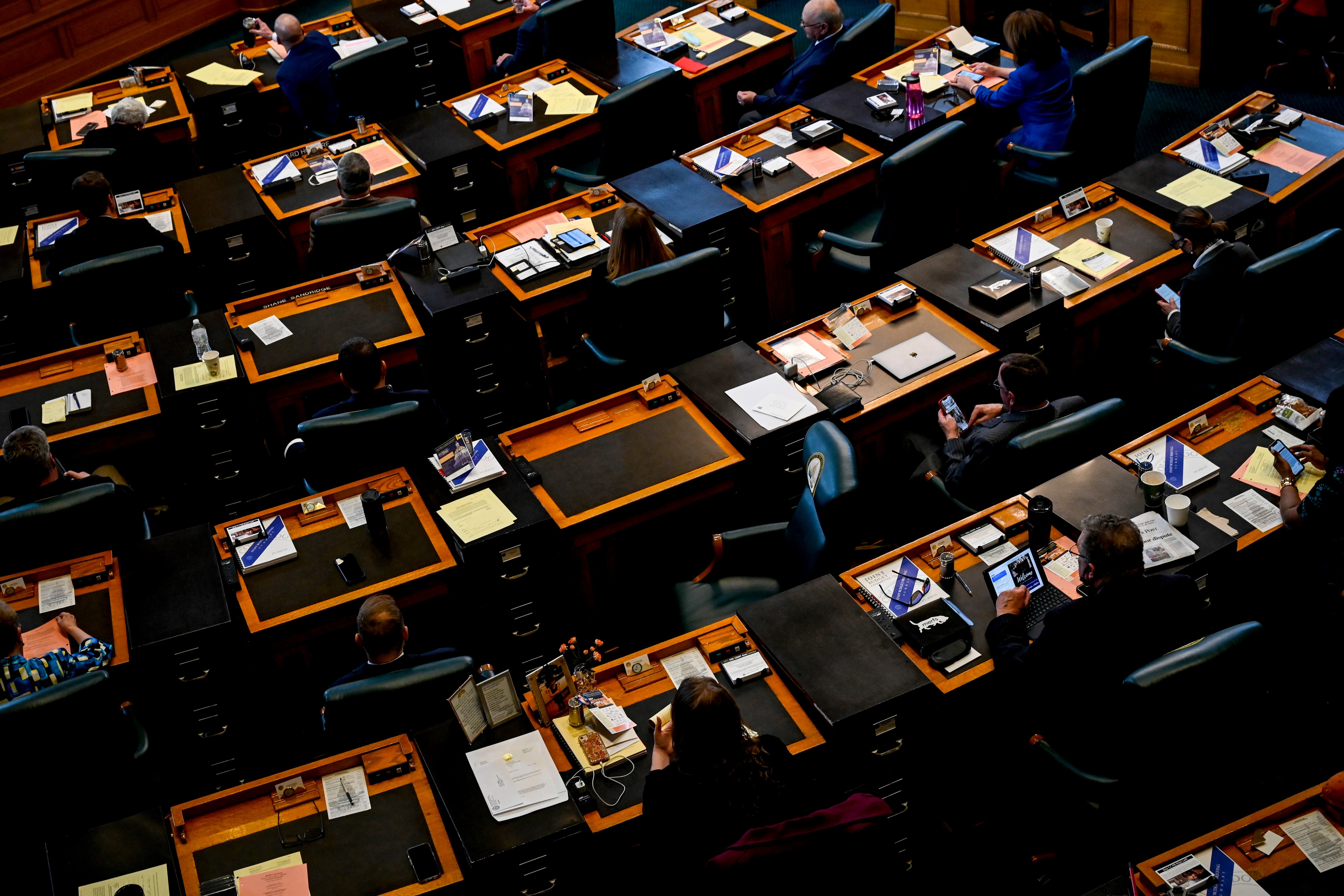 Colorado lawmakers sit at brown wood desks lined in rows in the state’s House of Representative chambers.