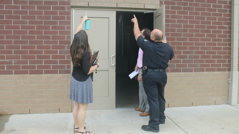 A police officer and a woman carrying a clipboard point overhead while inspecting a school doorway.