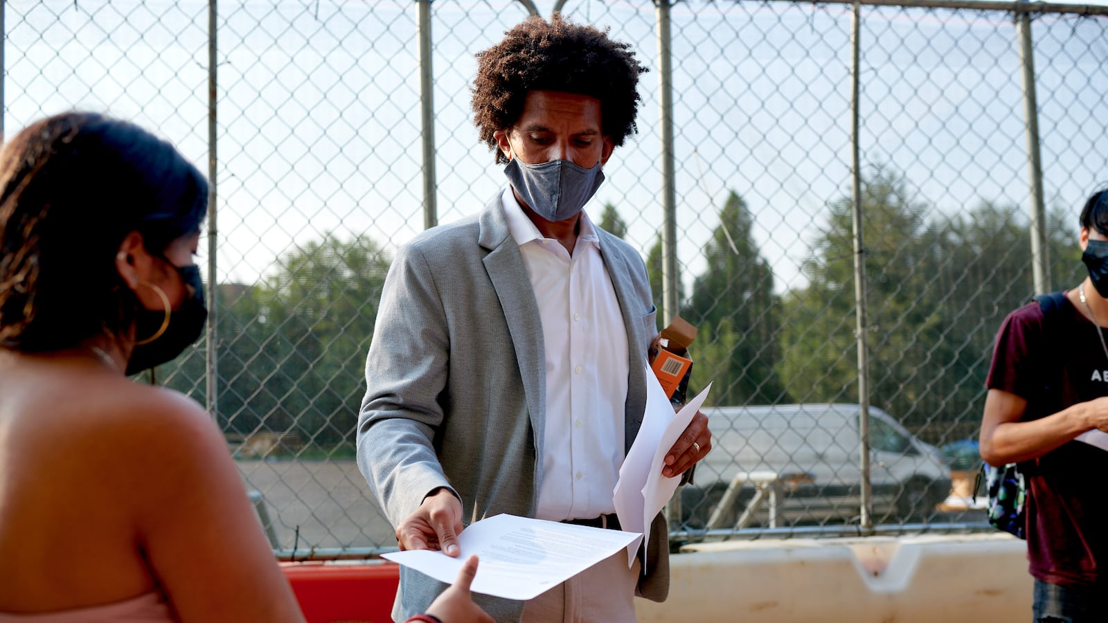 A school administrator in a grey suit jacket gives a COVID screening form from one of his students.