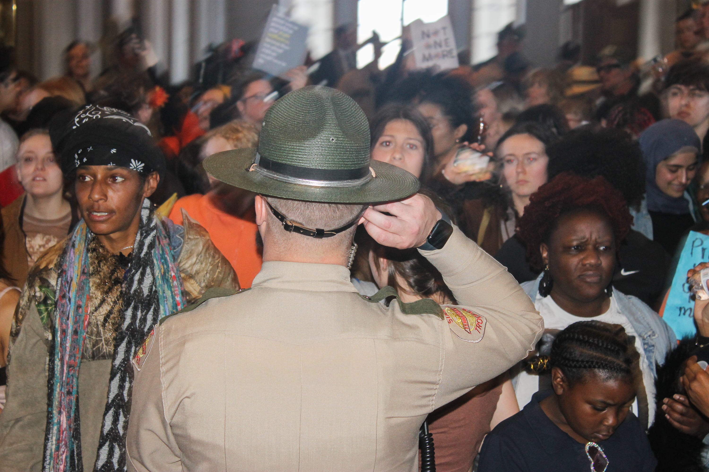 A law enforcement officer stands in front of a crowd of protesters.