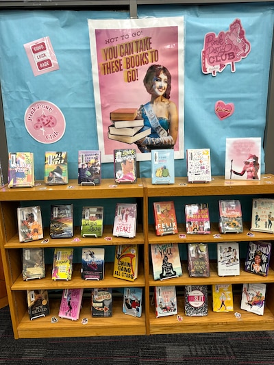 Books are on display in a school library with a blue and pink poster behind them featuring the singer Chappell Roan.