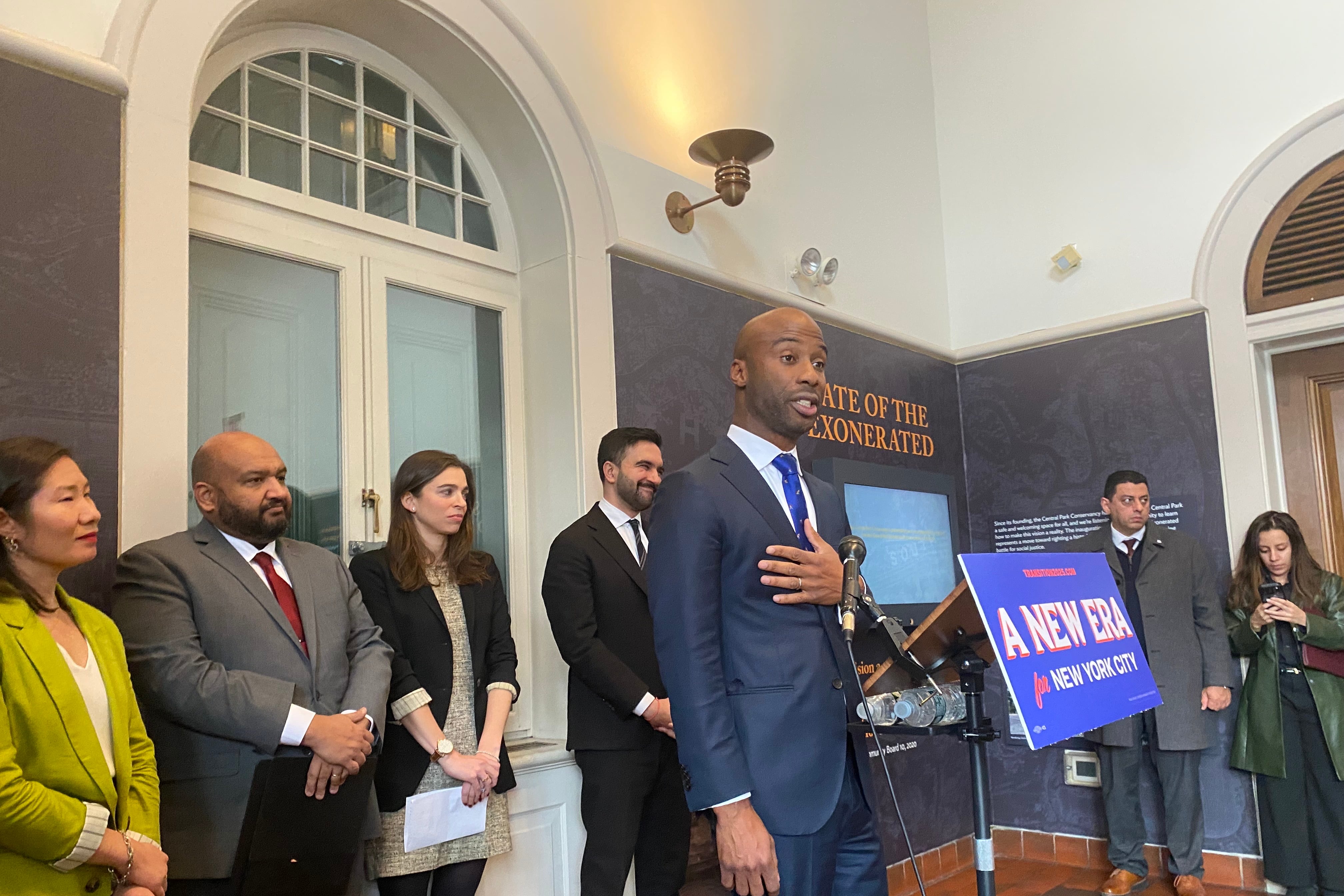 A man in a suit stands at a microphone.