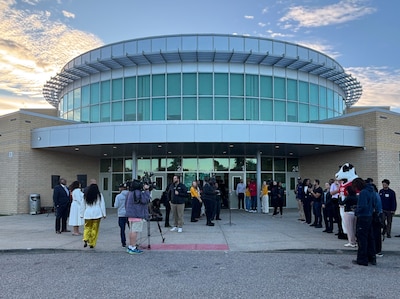 The front entrance of a large glass and stone high school building with adults standing outside.