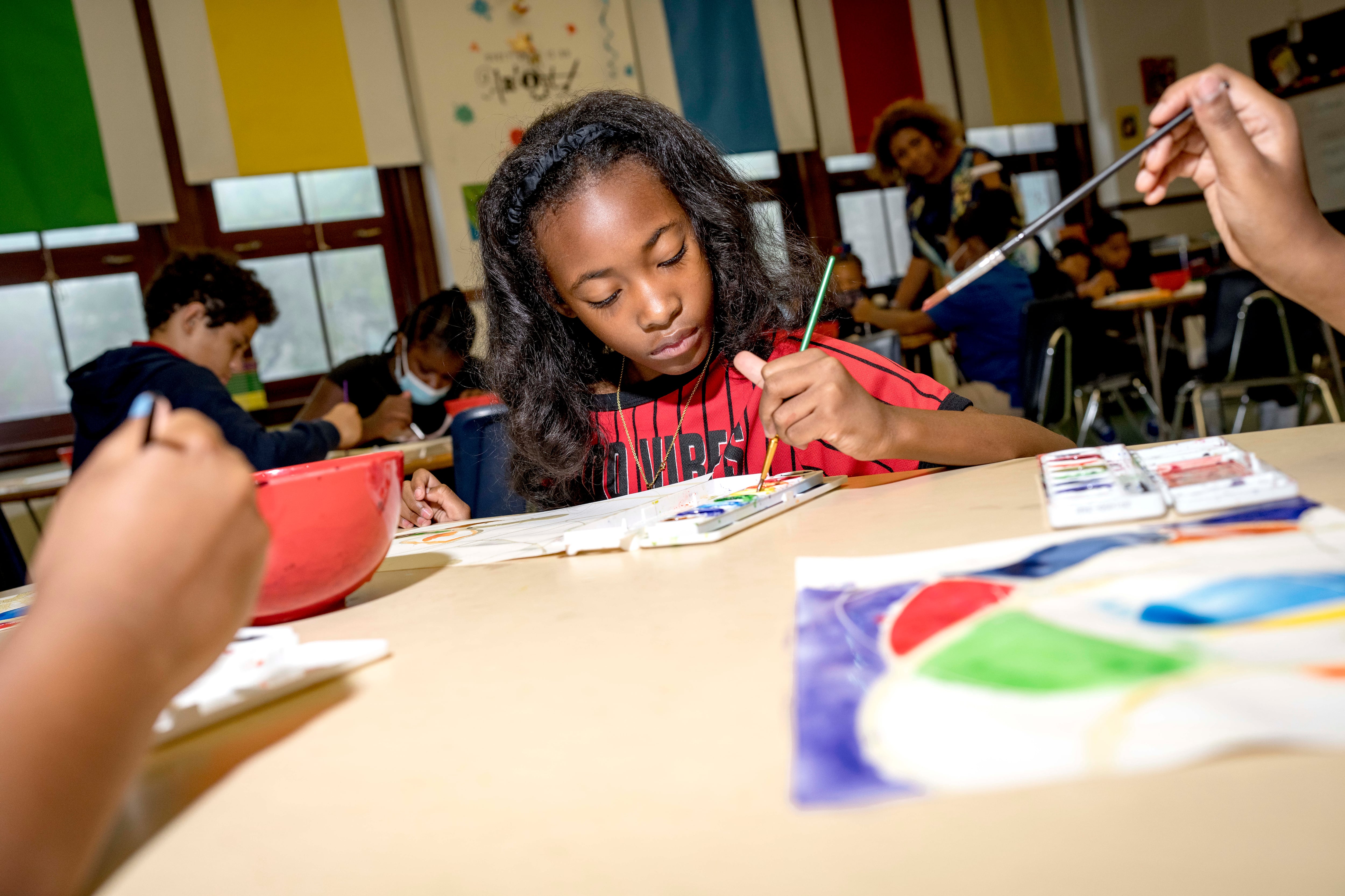 A student paints on a piece of paper in a classroom.