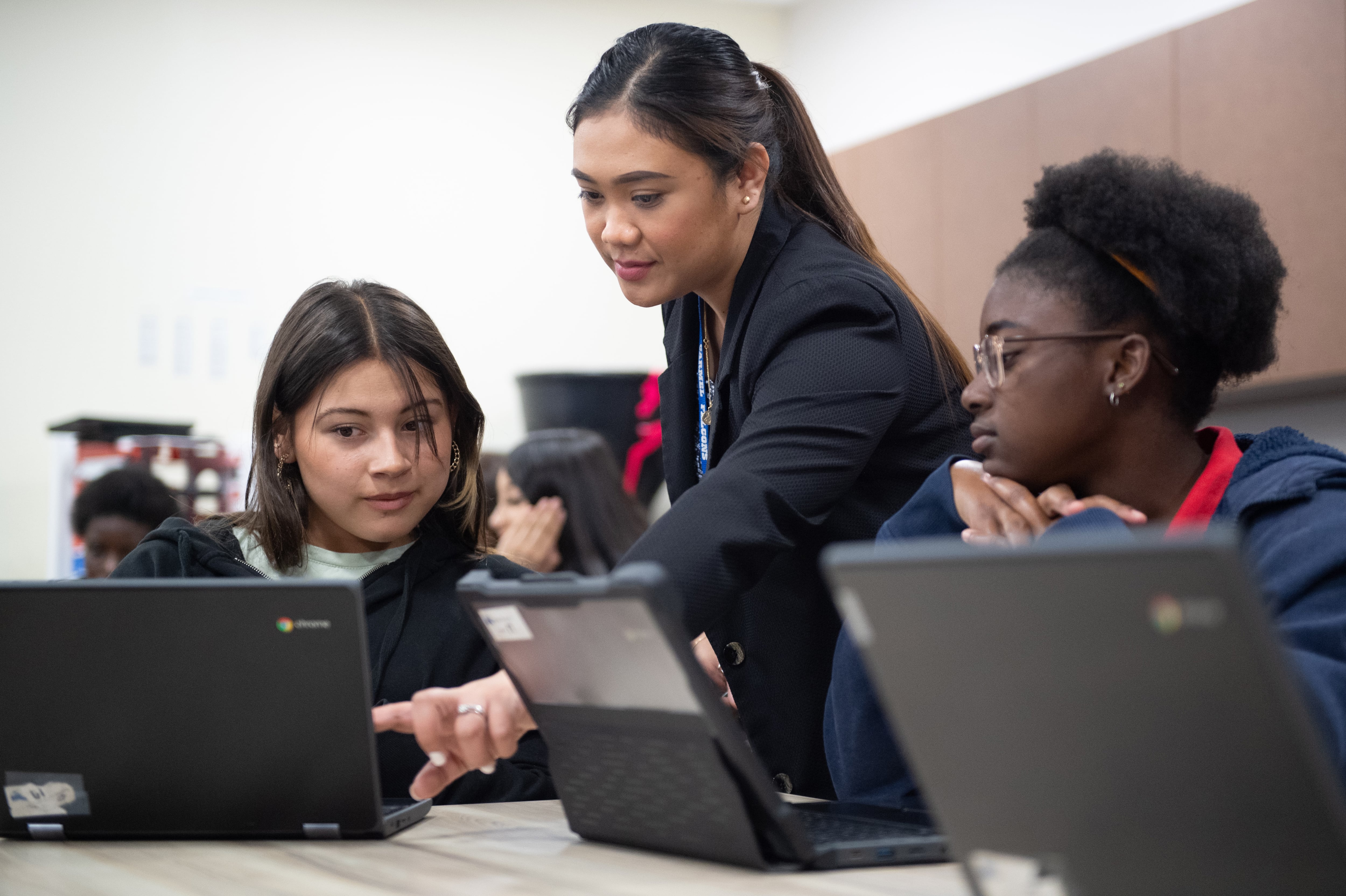 A woman with dark hair works with two students at computers