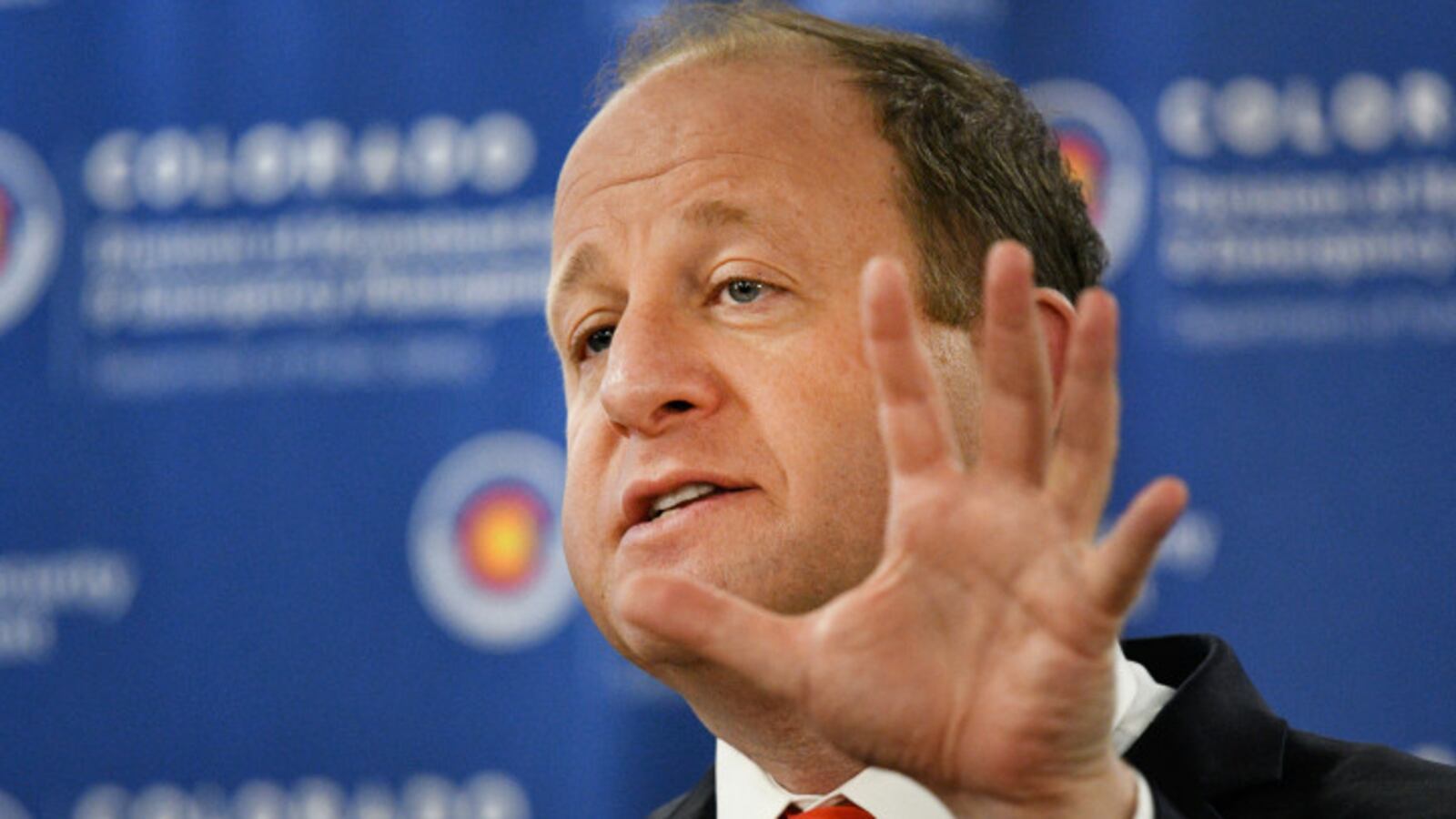Governor Jared Polis gestures with his hand while speaking.
