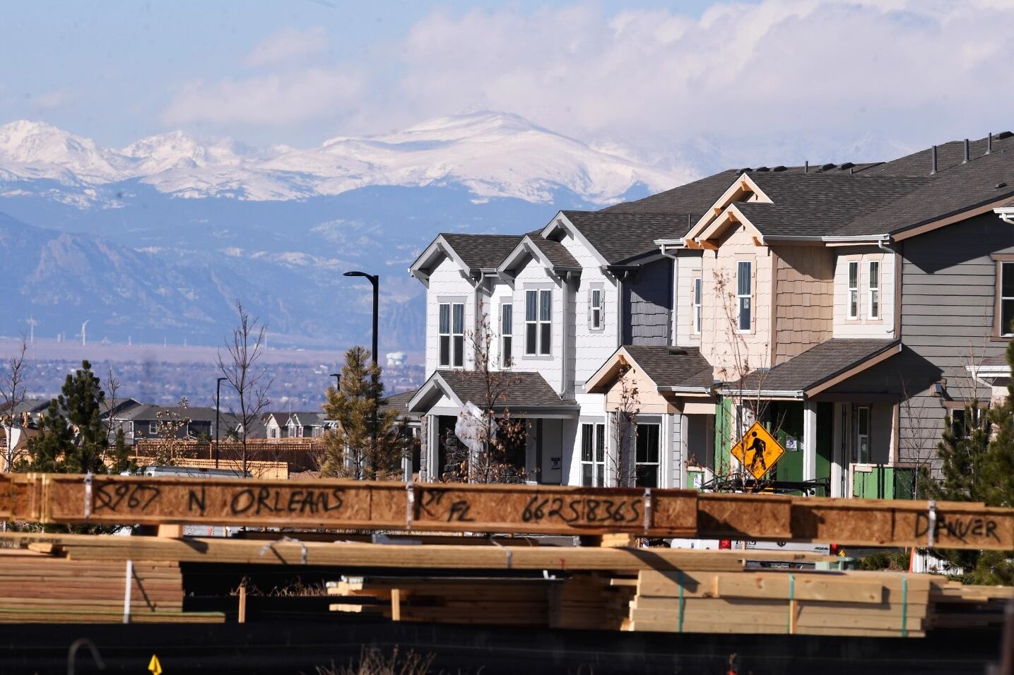 Homes in a newer subdivision stand in a line on the right side of the frame. On the left, the snow-capped Rocky Mountains can be seen in the distance.