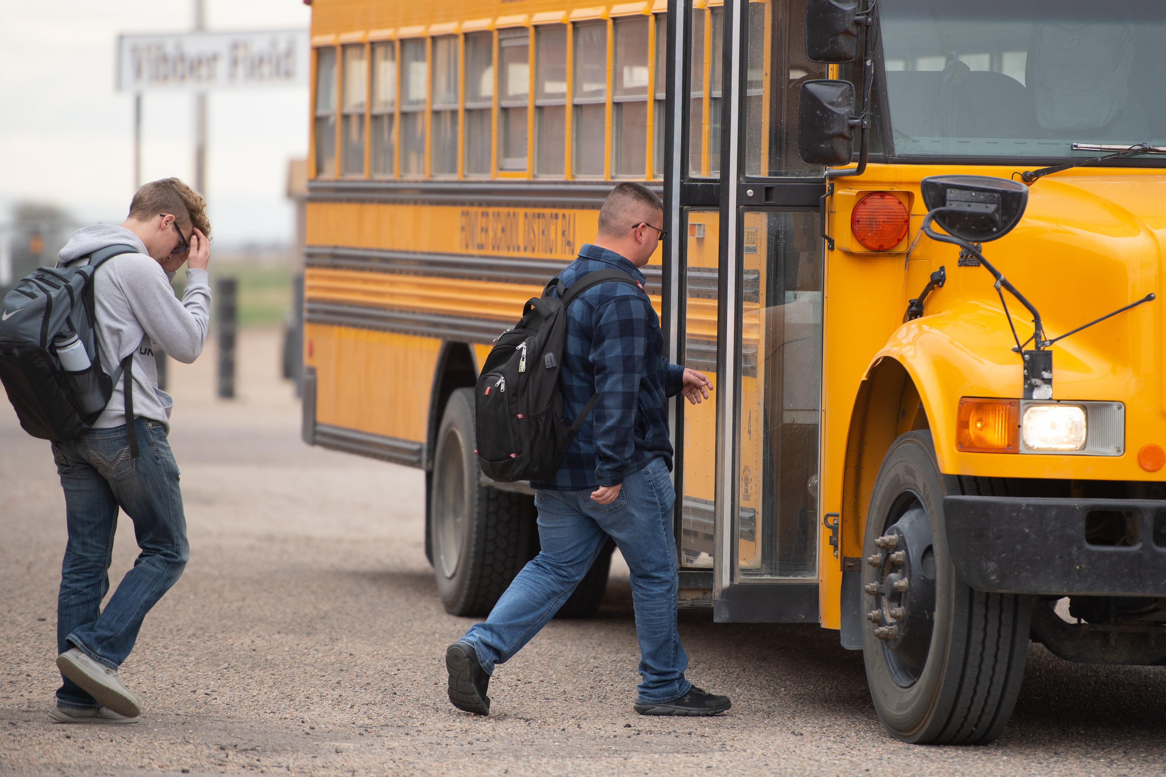 Two teenage boys in jeans and hoodies walk toward a stopped yellow school bus.