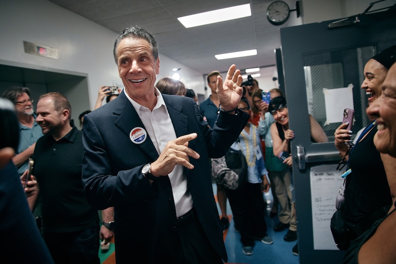 A man in a dark suit jacket holds his hands up in a crowded hallway.