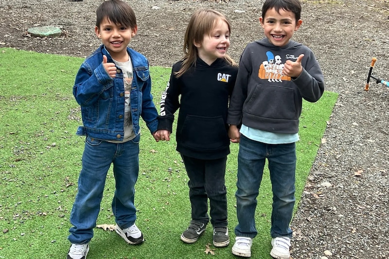 A photograph of three young children holding hands while playing outside.