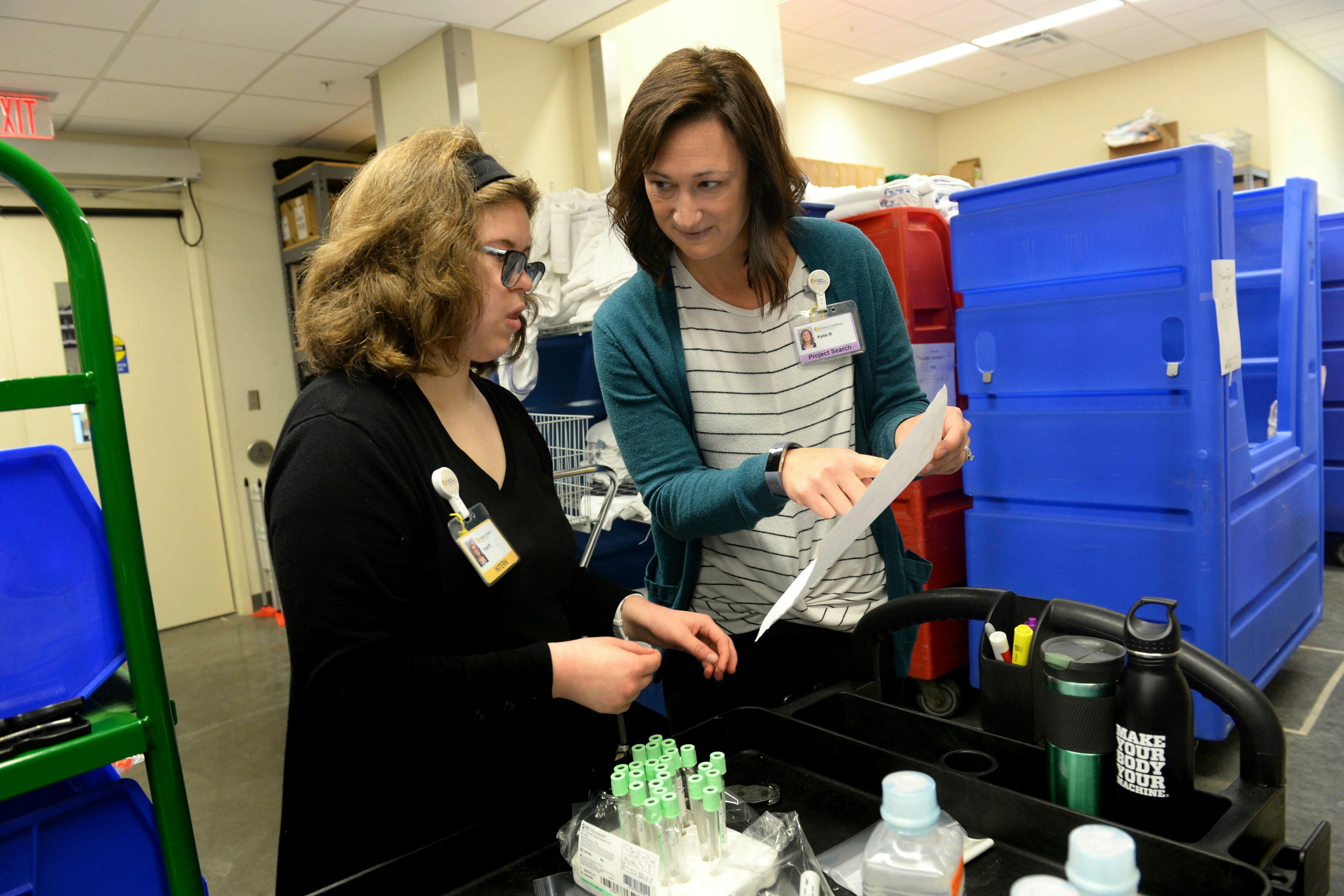 A young woman and an adult stand next to each other in a store working.