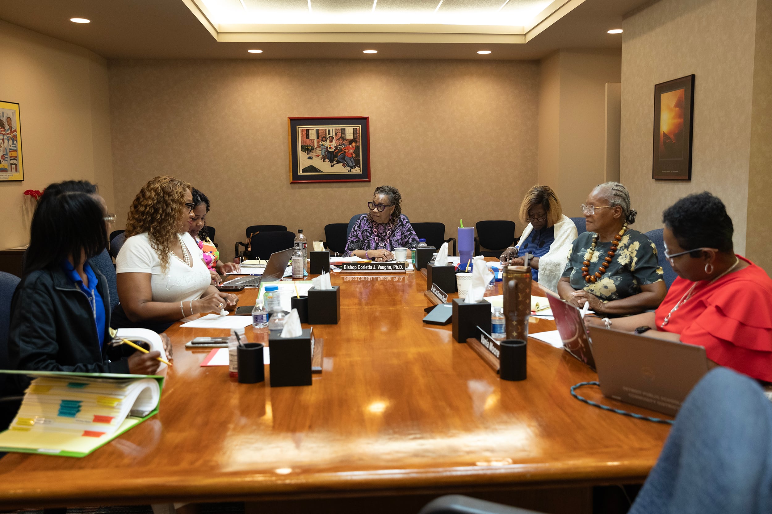 A room full of Black women in business clothes sit around a wooden table in a conference room.