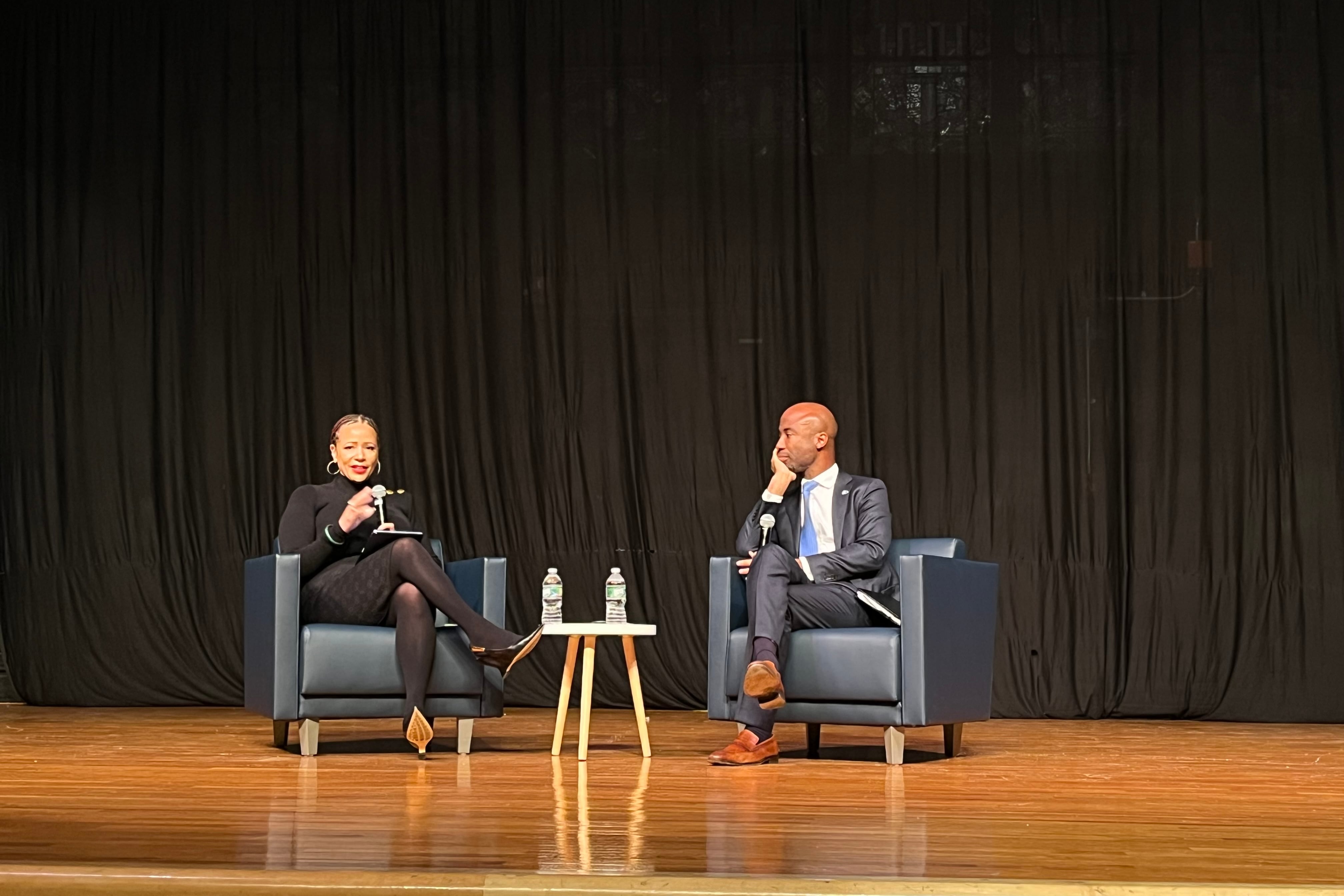 Two people sit on stage in conversation.