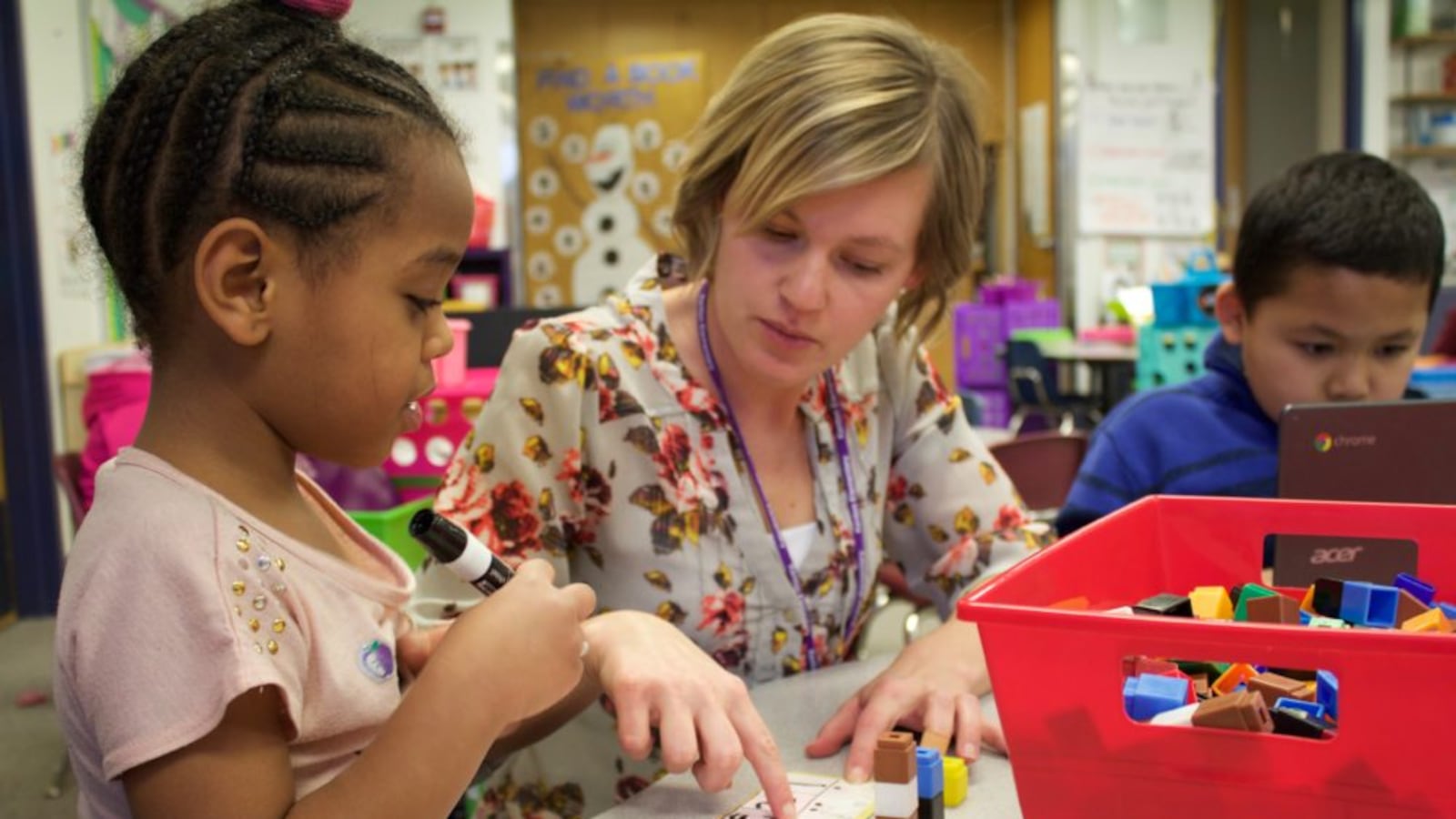 A kindergarten teacher at Kenton Elementary in Aurora, Colorado helps a student practice saying and writing numbers.