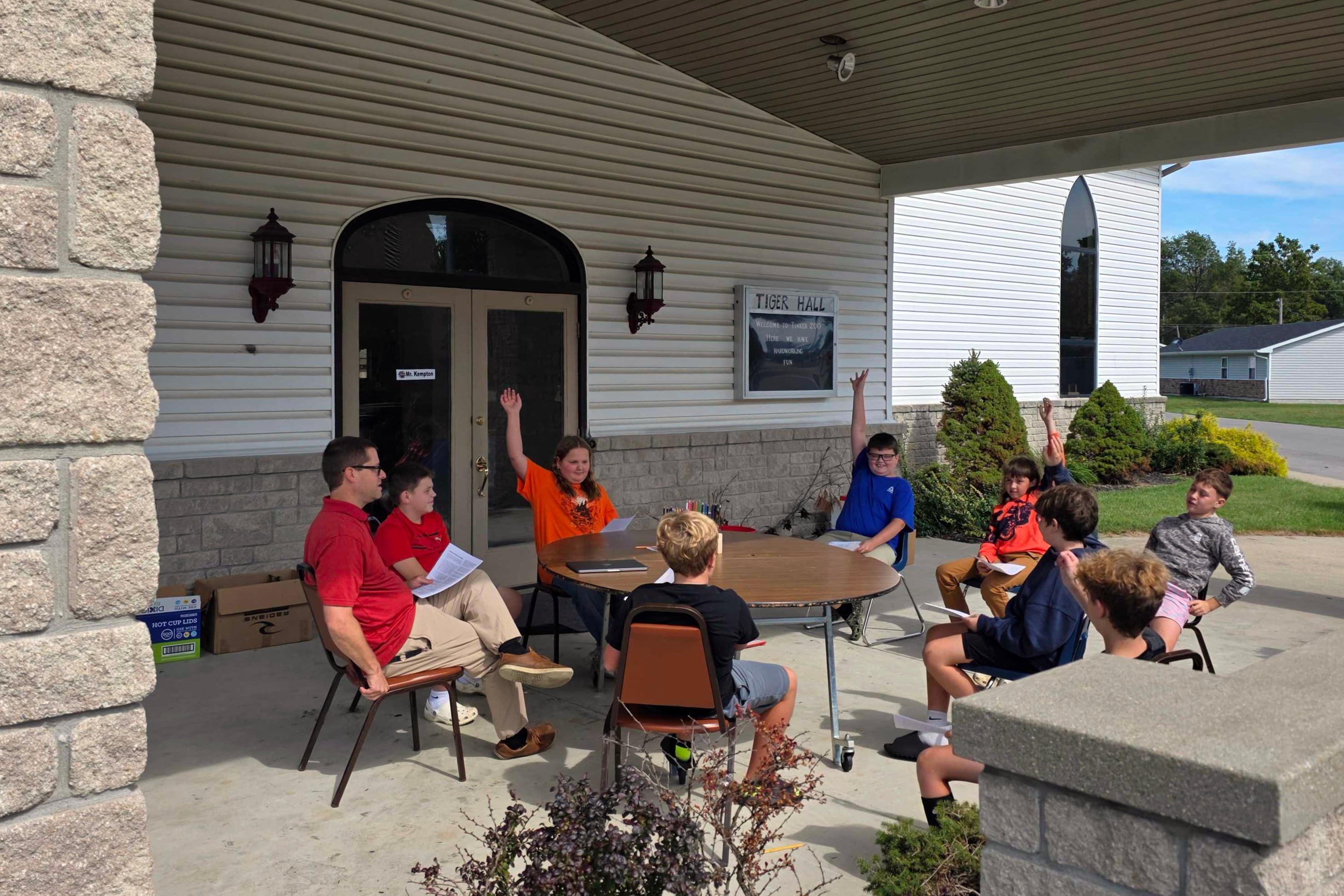Students and a teacher sit around a circular table outside.