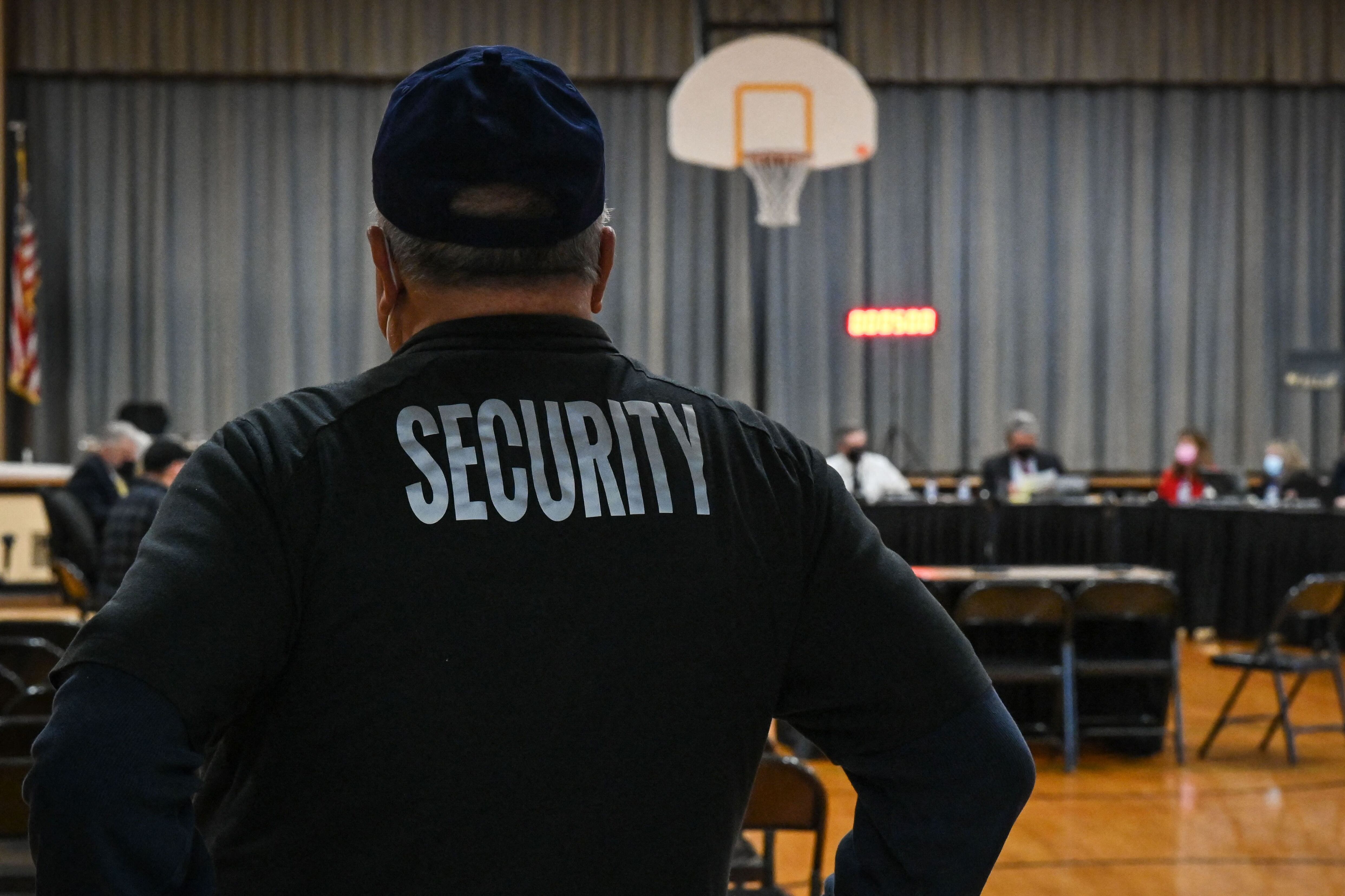 A security guard has he backed turned to the camera as faces a panel of speakers.