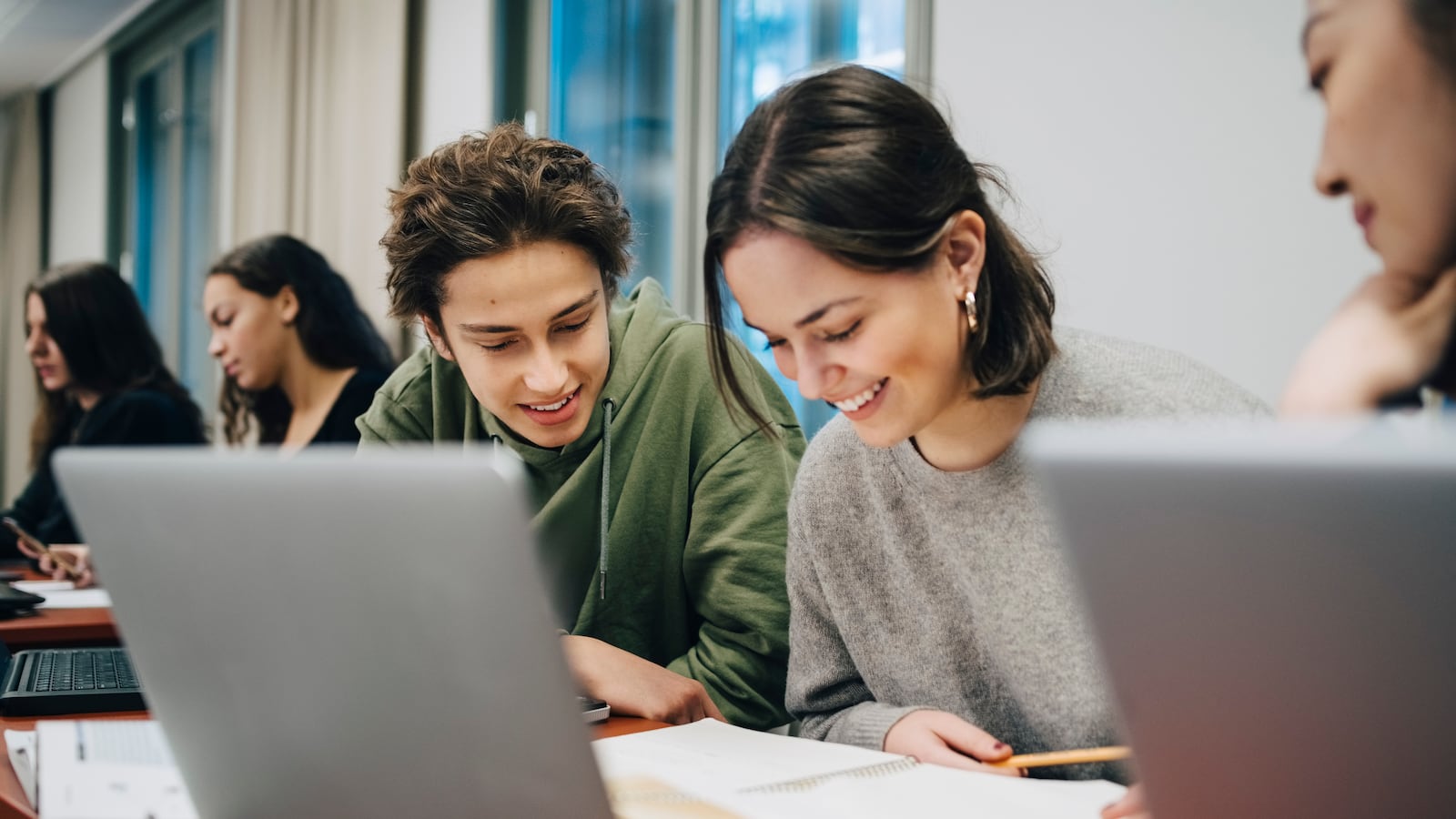 A group of high school students collaborate in class. They have laptop computers on the table.