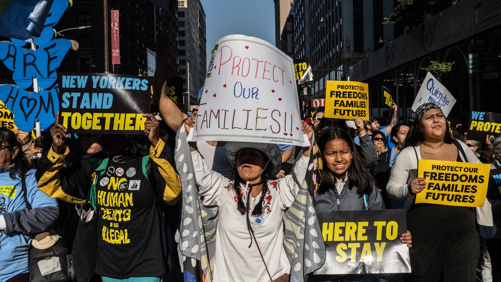 A group of people march in New York City, holding signs in support of immigrant rights.