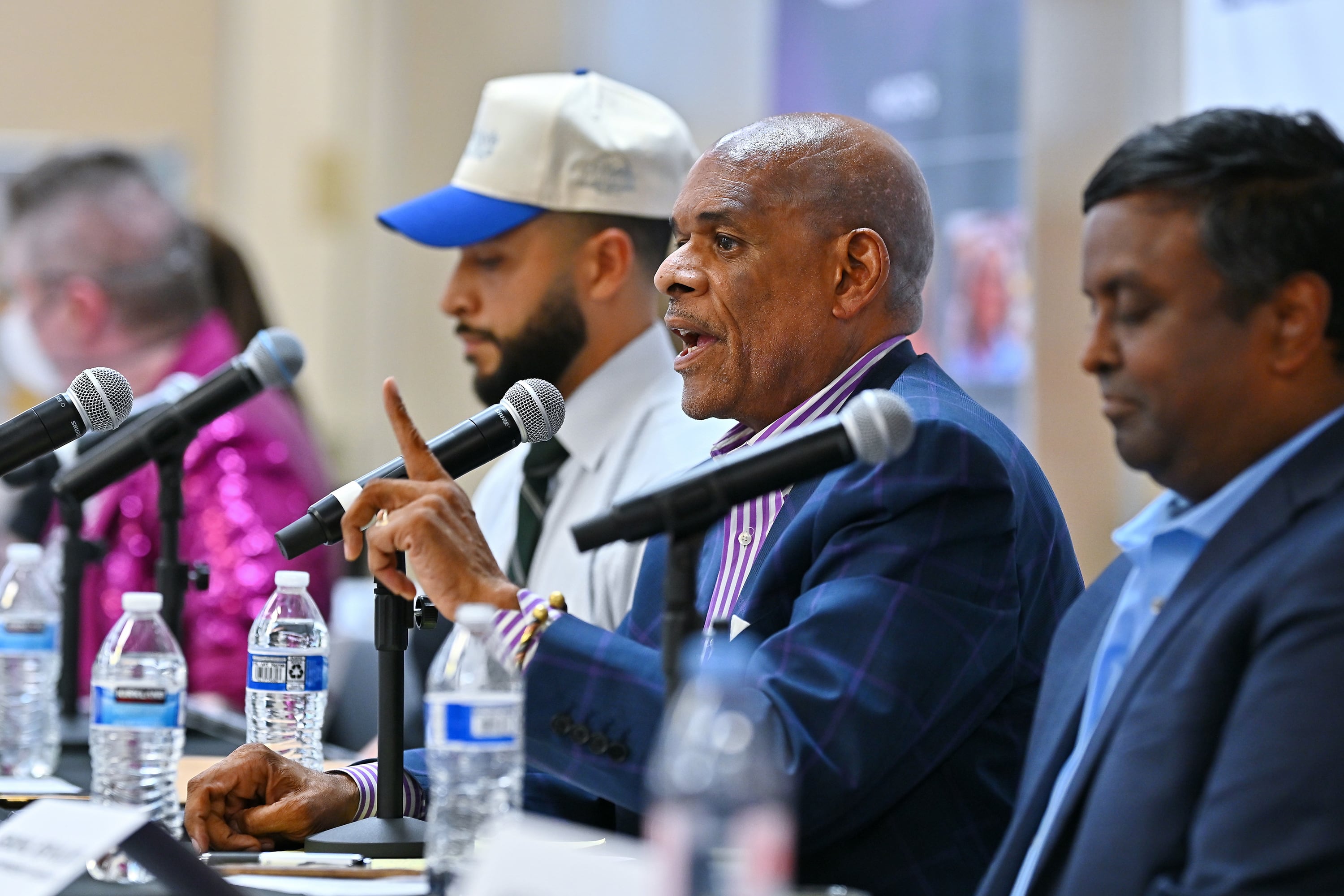 Three men in business clothes sit at a table lined with microphones.