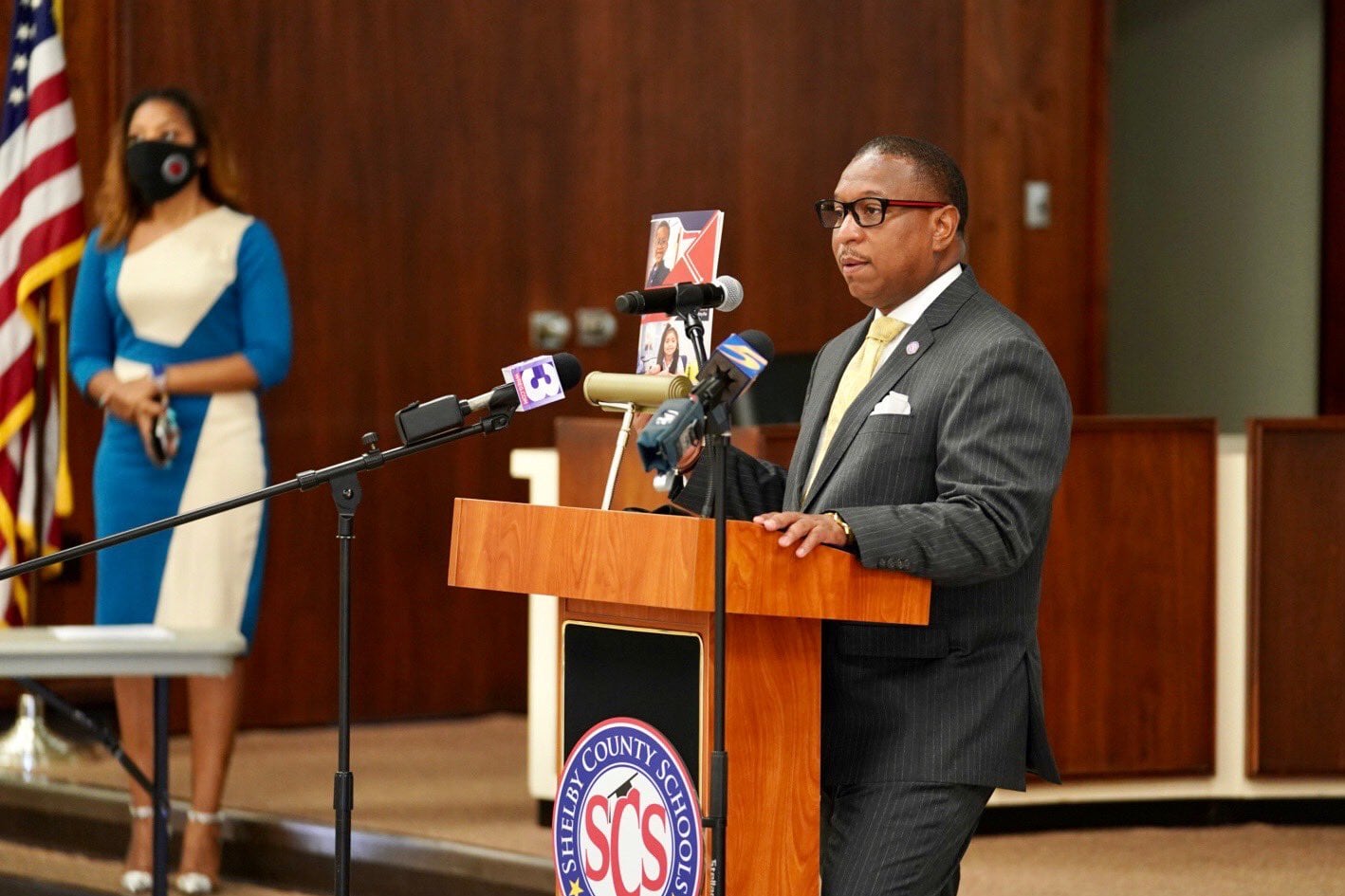 Superintendent Joris Ray speaks with reporters in 2020. He stands behind a podium in a gray suit and glasses.