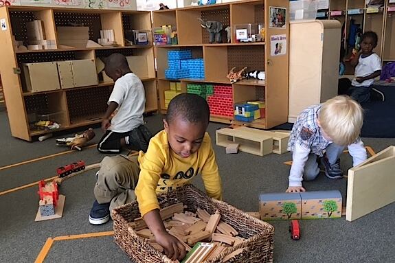 Four young children are playing on the ground with toys in a classroom.