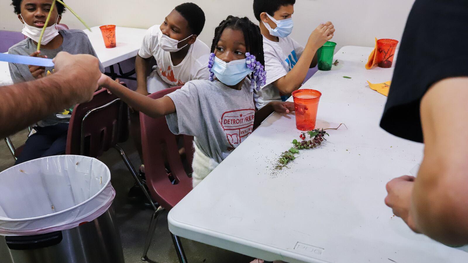 Students work with seeds picked up during a seed walk outside of their class. A girl shows some of the ones she found to a teacher in their classroom.