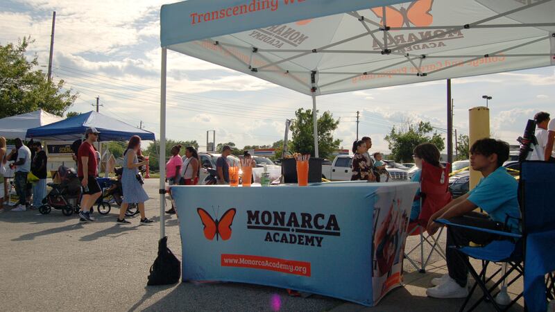 A blue tent with orange butterflies is set up at a festival with patrons walking around. People sit in the shade under the tent.