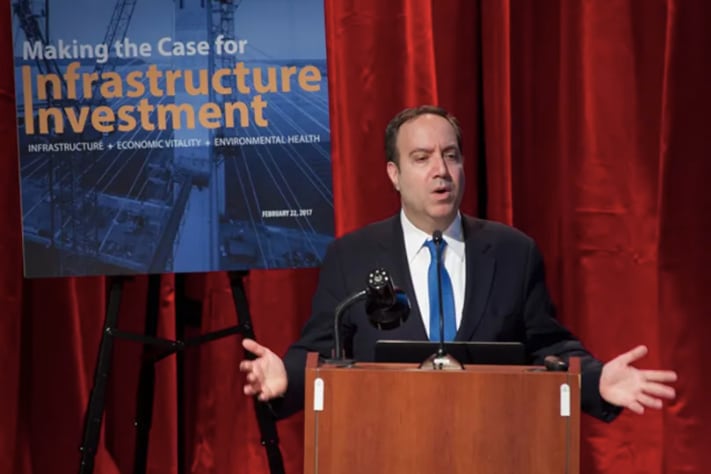 A man in a suit stands in front of a red curtain.